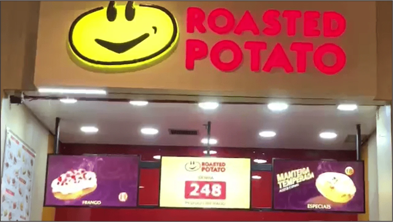 Fachada do Roasted Potato com três televisores, laterais exibindo mídias e central chamando senha