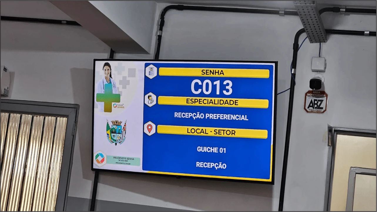 Ambiente de saúde com televisão chamando senha C013 para guichê 1 recepção preferencial