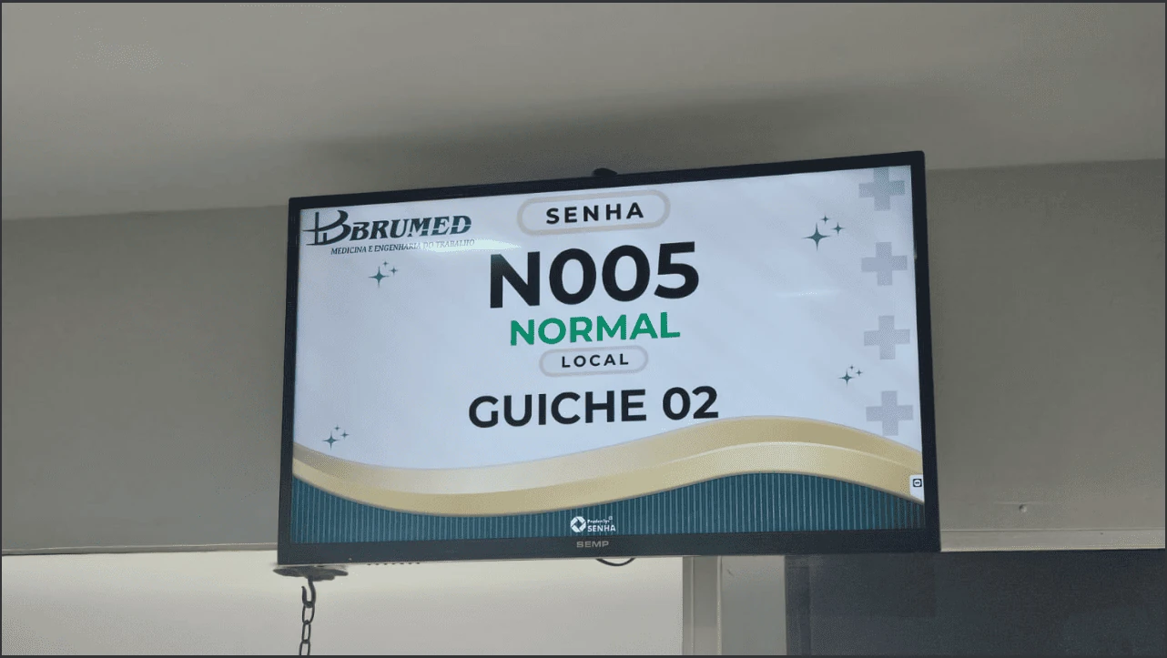 Interior da clínica Brumed com televisão chamando uma senha