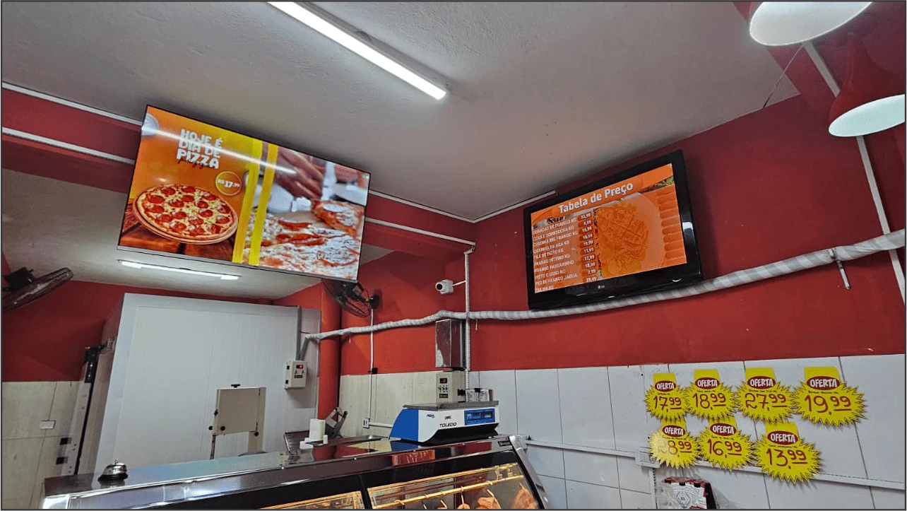 Interior de supermercado com televisão exibindo 'Hoje é dia de pizza' e tabela de preços